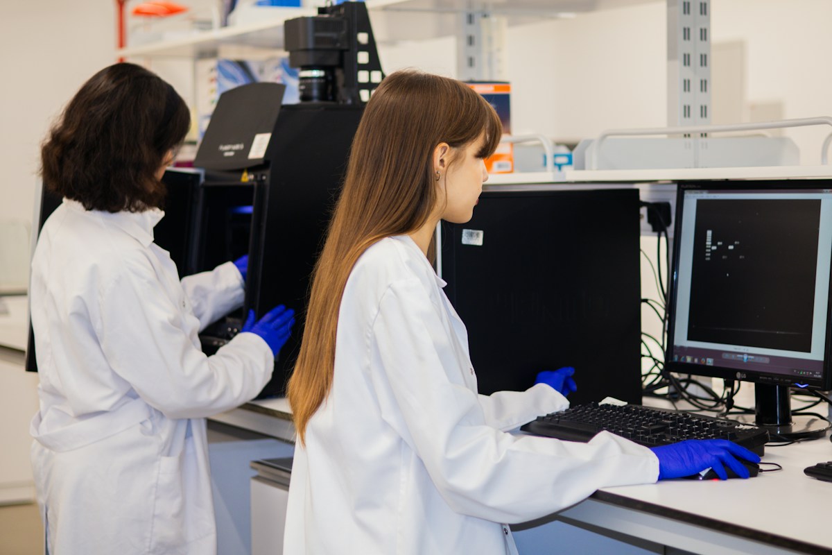 Two researchers in lab coats and gloves working at laboratory instruments